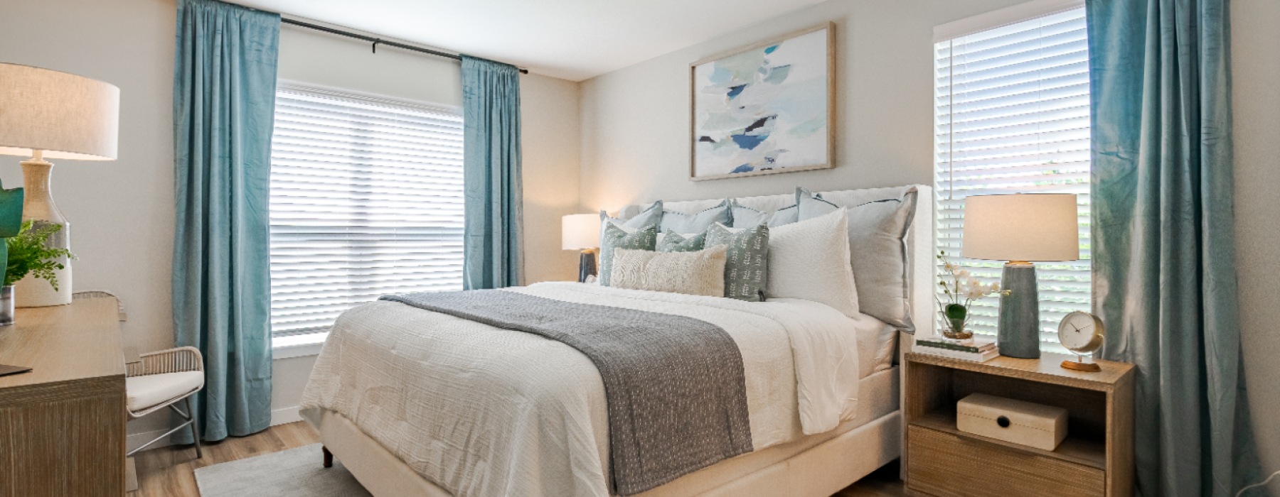 swath of sunlight shines across a well made bed and bedside table with a vase of cotton plants