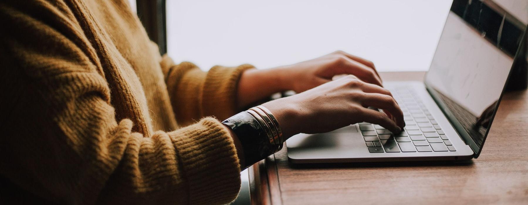 woman types on her laptop near large window